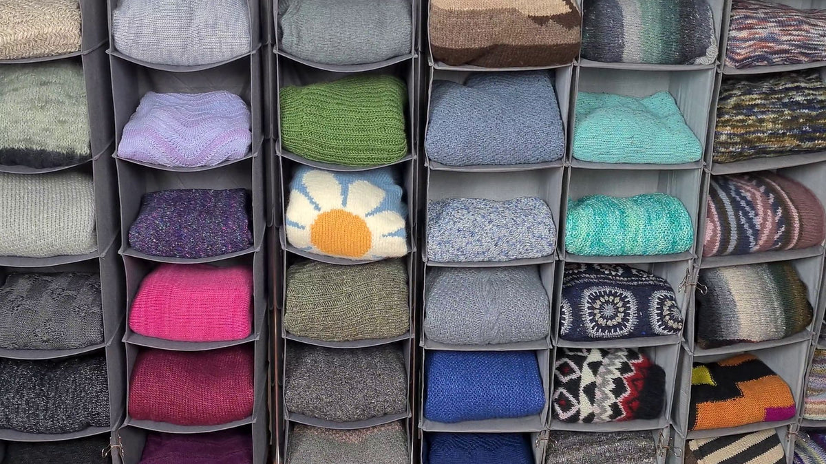 Gefaltete Strickpullover liegen einzeln in offenen Stoffregalen