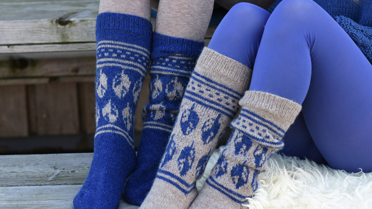 Zwei getragene Sockenpaare in Blau und Beige mit geometrischem Muster auf einer Holzbank.