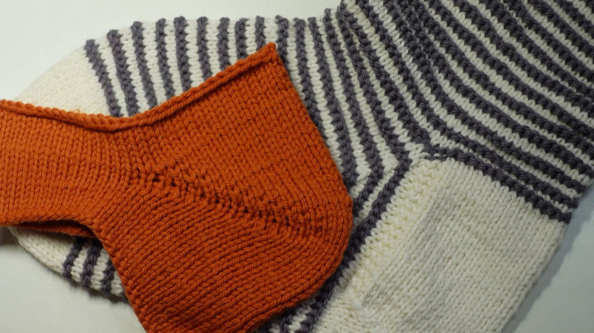 Gestrickte Bumerangferse in Orange vor einer geringelten Socke