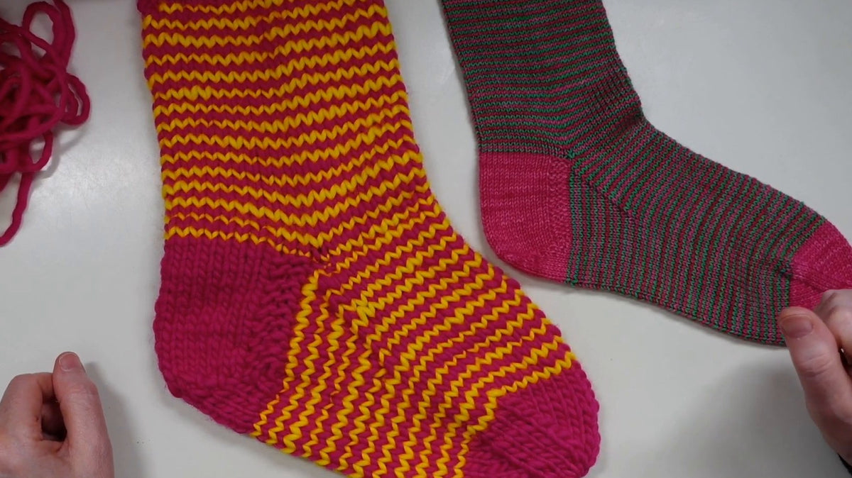 Fertige Ringelsocke mit pinker Bandspitze neben einer zweiten Socke