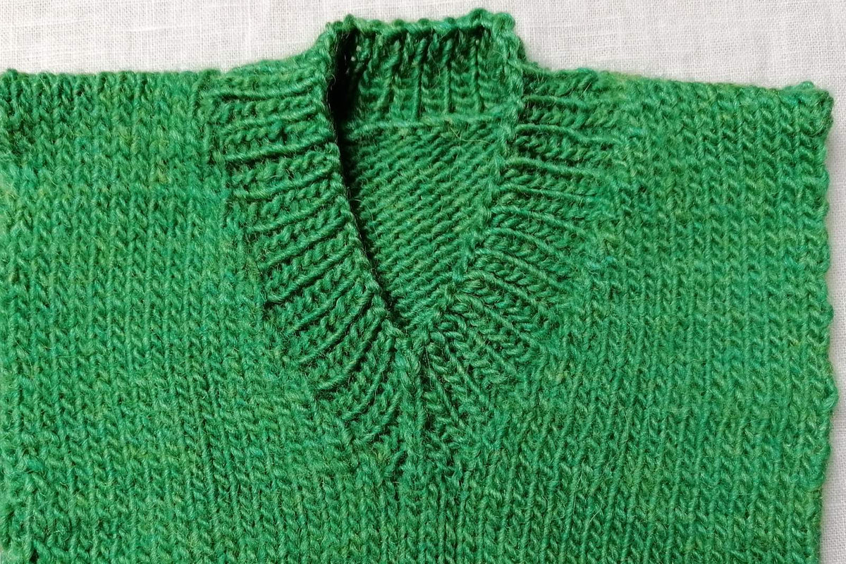 Grüne V-Ausschnitt-Probe mit Rippenblende und betonter Spitze.