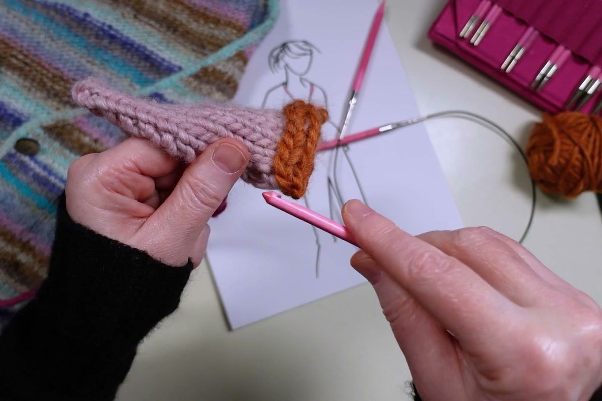 Orangefarbene I-Cord-Kante am Rand einer rosafarbenen Strickprobe.