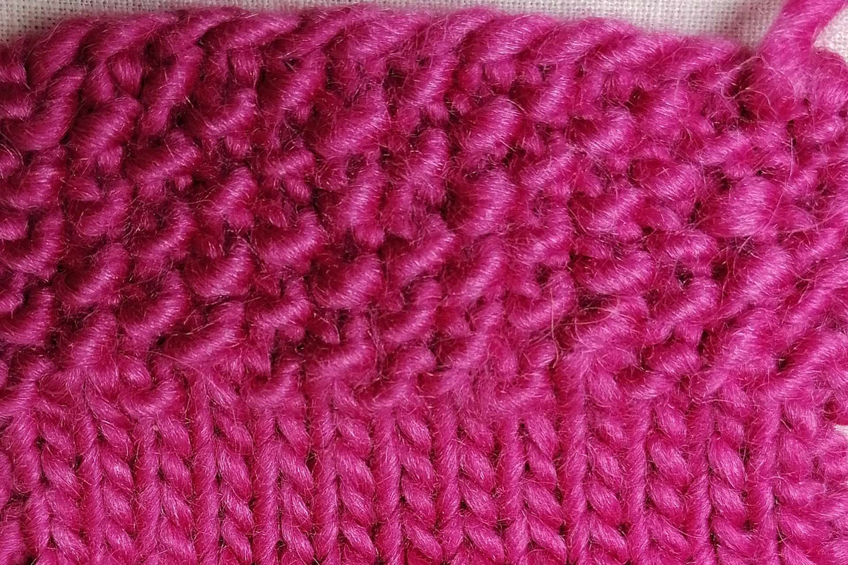 Magentafarbene Strickprobe mit kleinem Perlmuster über glatt rechts