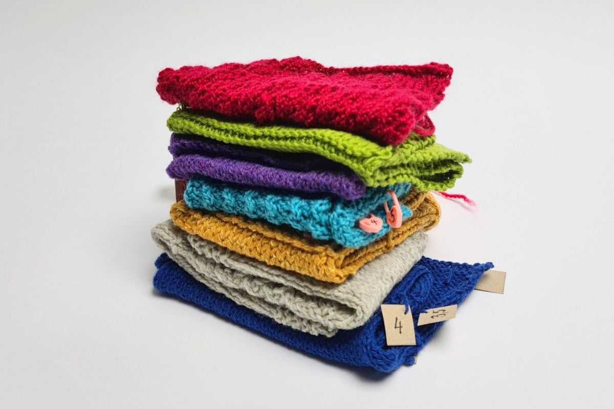 Stapel bunter Strickproben in Rot, Grün, Lila, Türkis, Senfgelb, Hellgrau und Blau