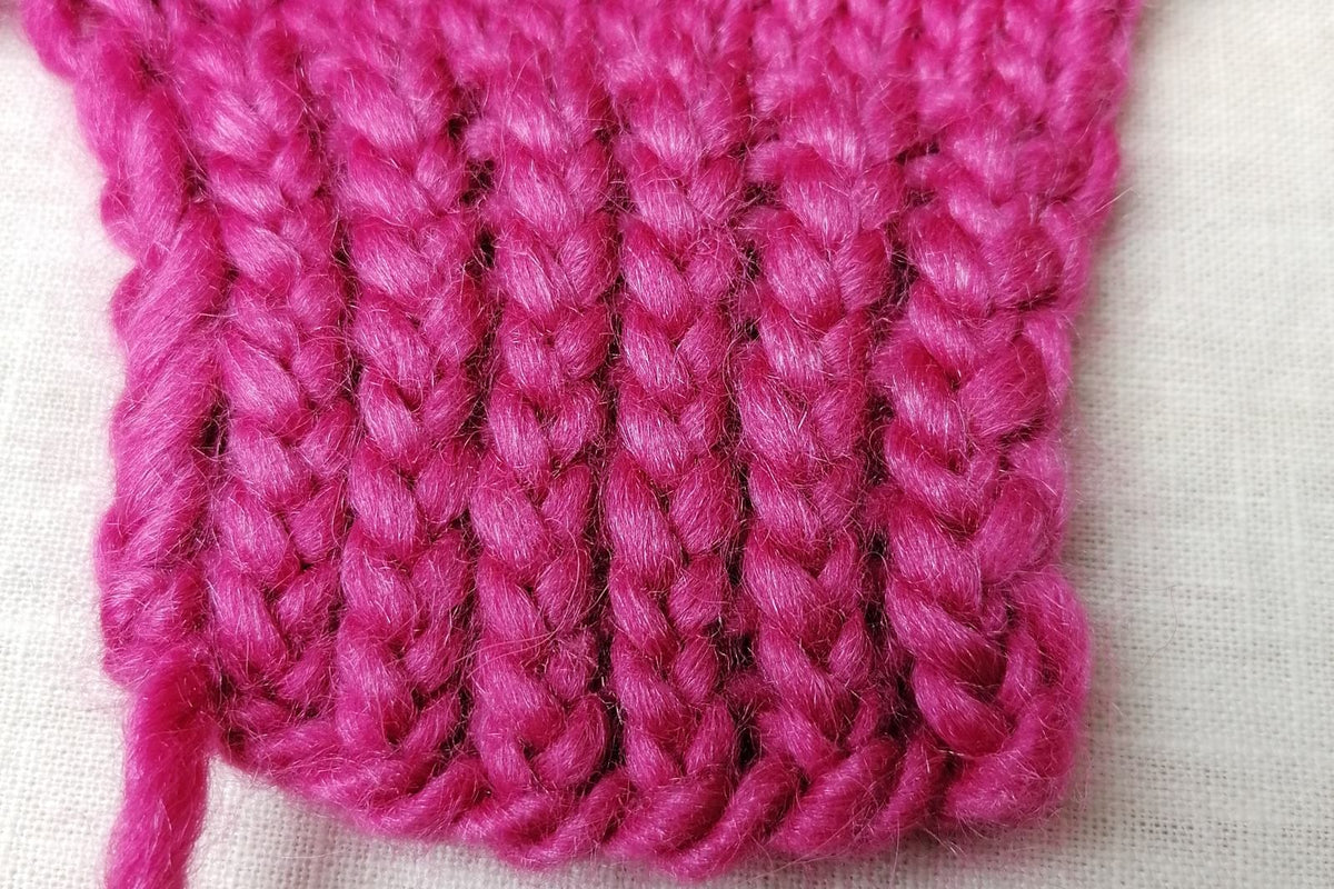 Pinkfarbene Rippenprobe mit verschränkten Maschen in Nahaufnahme.