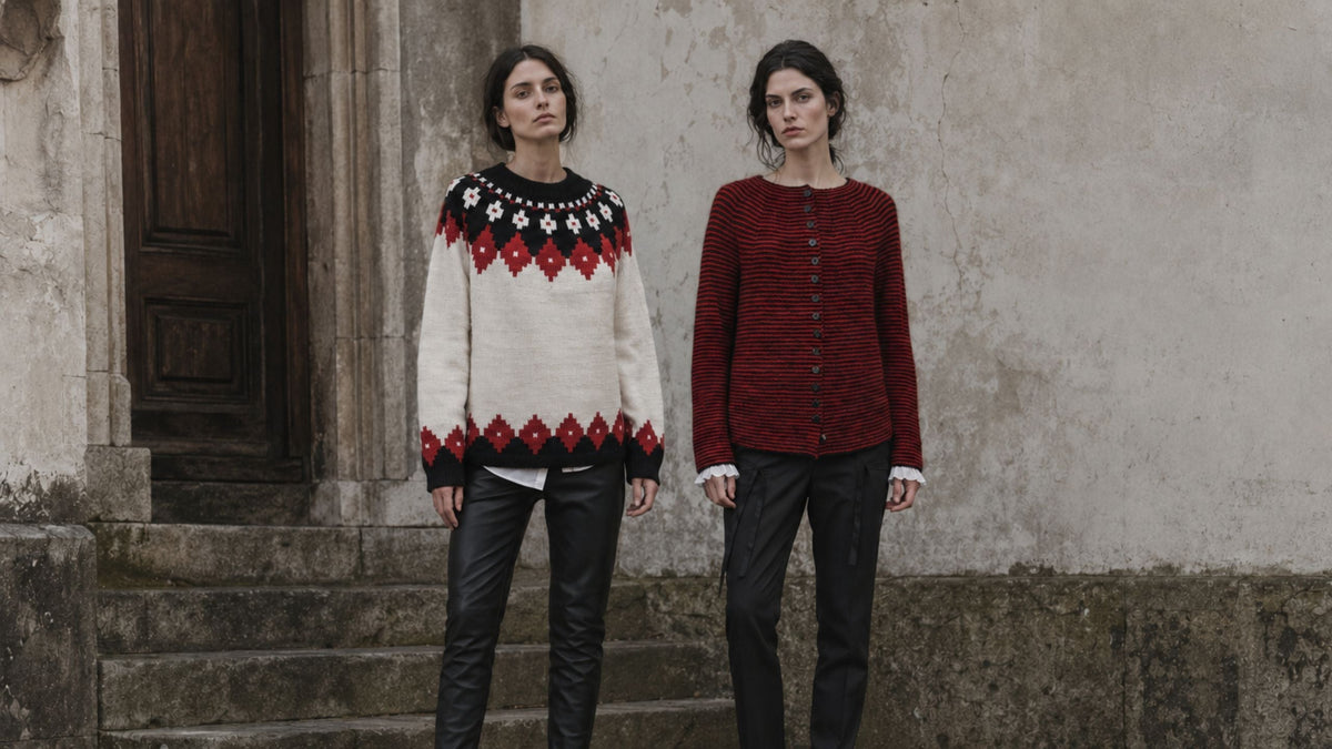 Zwei Frauen vor verwitterter Steinmauer, eine im creme-roten Rundpassenpullover, eine in rot-schwarzer Jacke