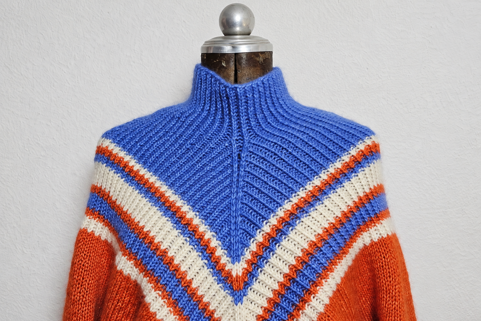 Pullover Witch auf einer Schneiderbüste: blauer Kragen und V-förmige Streifen in Blau, Naturweiß und Rostrot, Querformat-Ausschnitt