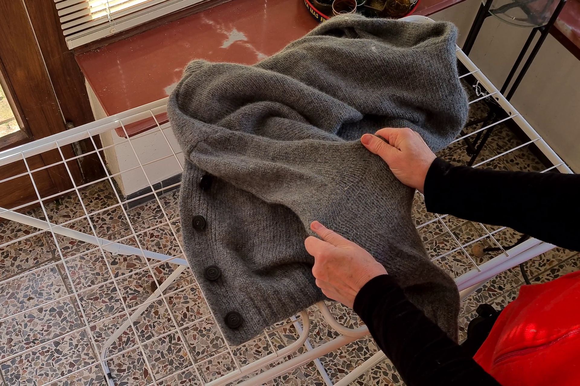 Verfilzte graue Strickjacke wird auf dem Wäscheständer von Hand gedehnt
