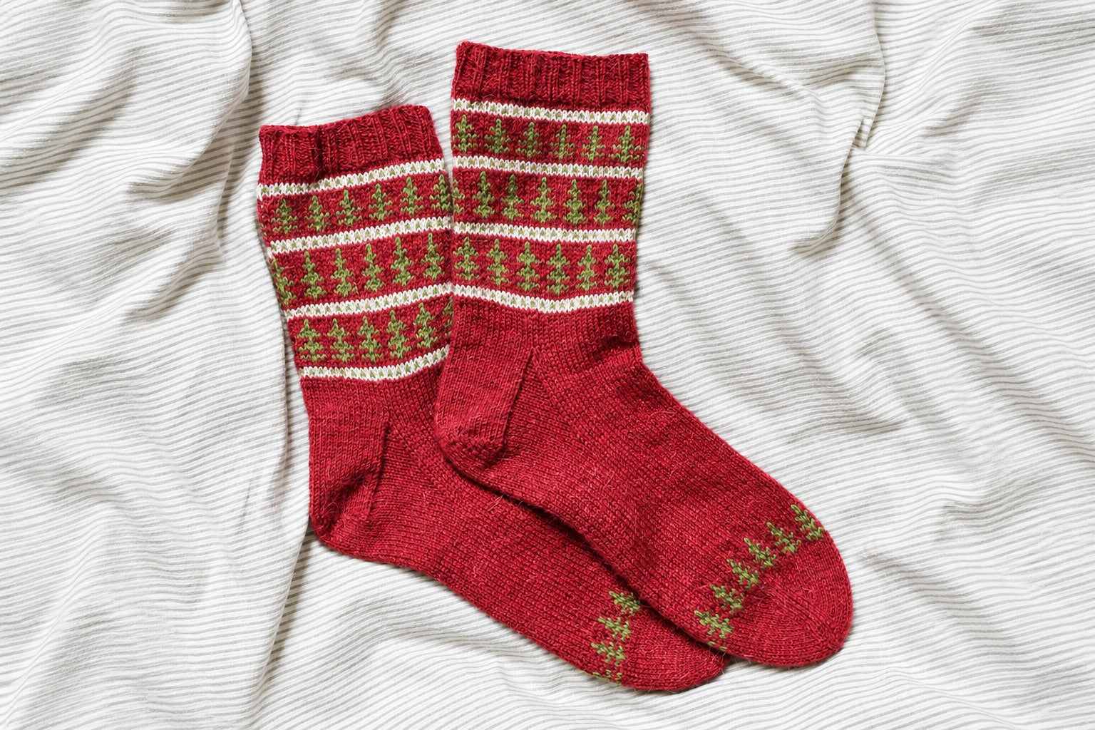 Zwei rote Socken Tannenparade mit grünen Tannen und weißen Streifen auf gestreiftem Stoff. Hintergrund für das Querformat mit KI erweitert.