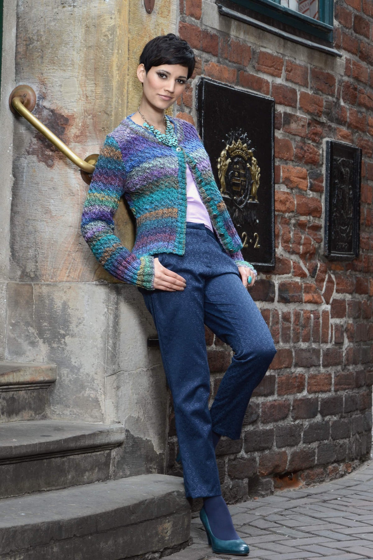 Kurze Jacke Chloe aus buntem Verlaufsgarn mit Fallmaschenmuster und acht Knöpfen.